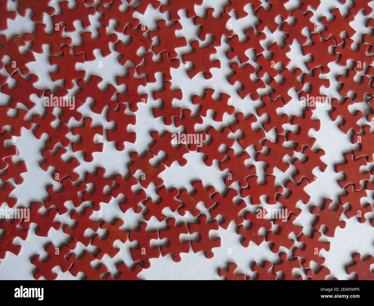 Eine Masse von Puzzleteilen auf dem Tisch, die alle die gleiche Form und Farbe von Rot aussehen. Stockfoto