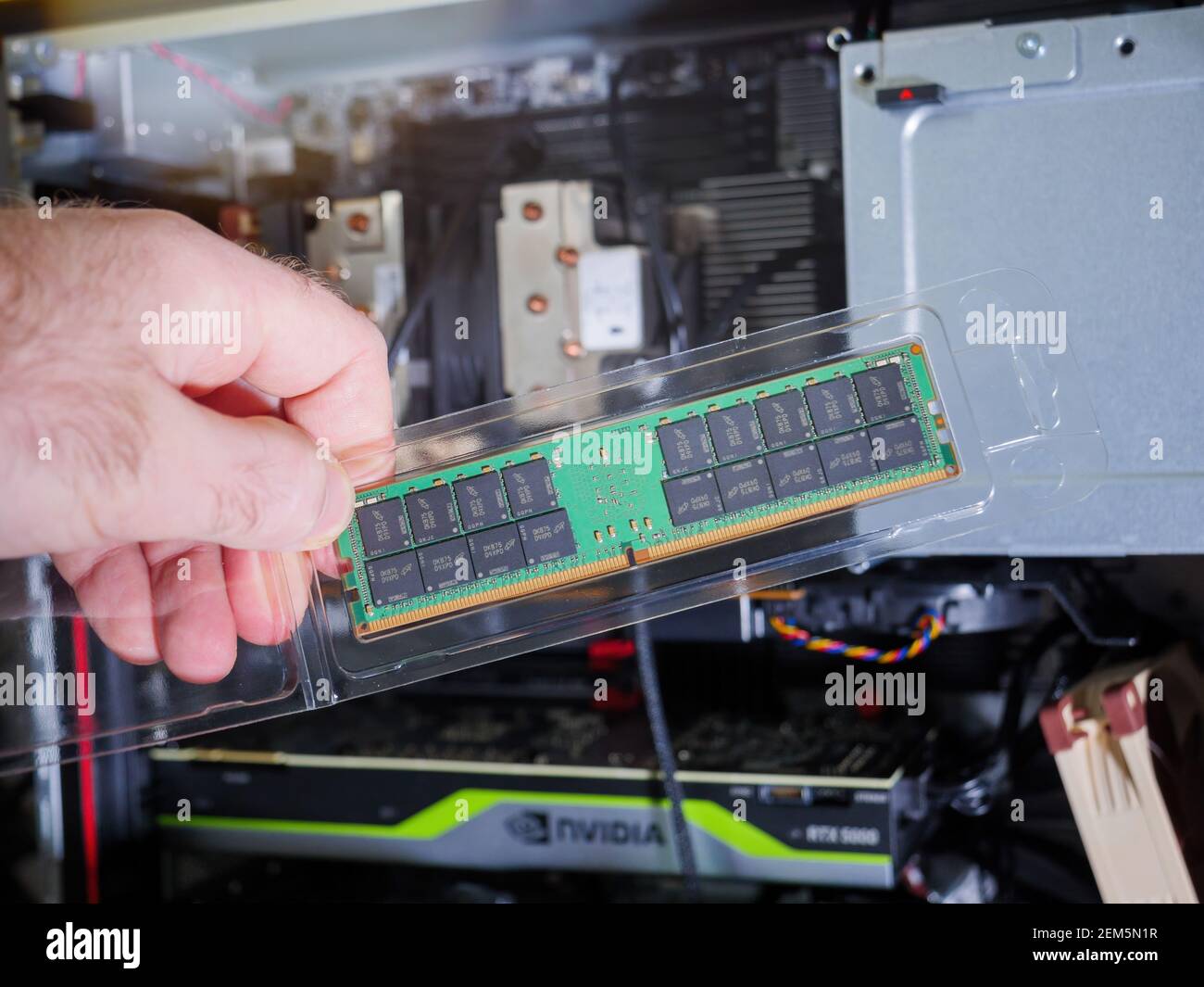 Paris, Frankreich - 4. Feb 2021: POV männliche Hand hält Blick auf das neue Paket von Micron 64GB DDR4 RDIMM RAM Random Access Memory mit einem leistungsstarken Computer im Hintergrund Stockfoto