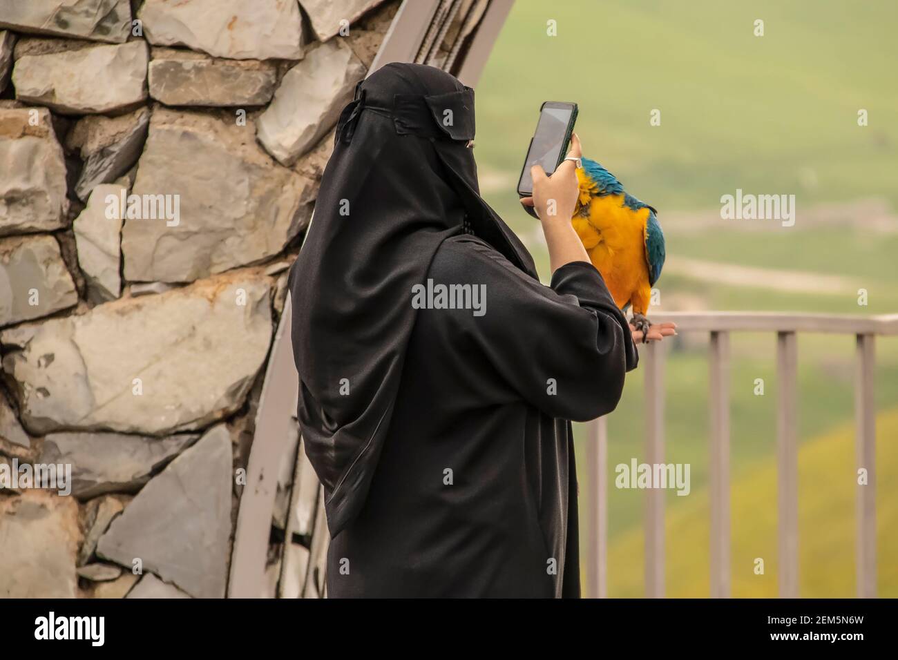 Frau in Krepp texturierten Burka bei szenischen Ausblick Foto machen Mit einem Smartphone eines Papagei hält sie - Selektiver Fokus Stockfoto