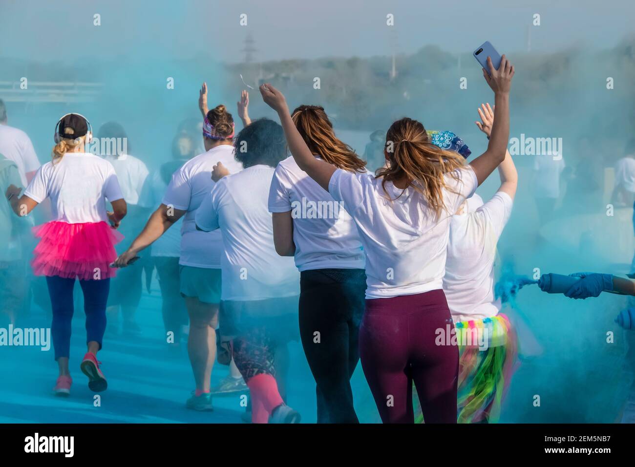 Frauen laufen in einem holi Farbe Rennen mit Waffen Aufgewachsen mit blauem Pulver, das um sie herum wirbelt - unerkennbare Menschen Stockfoto