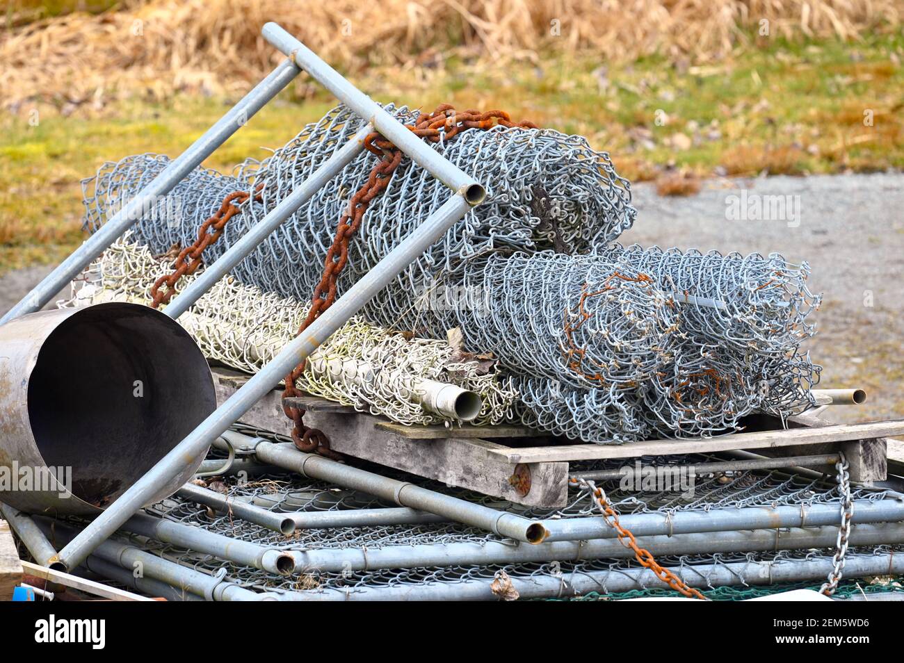 Ein Stapel aufgerollter, weggeworfener Kettengliederzäune mit einer verrosteten Kette. Stockfoto