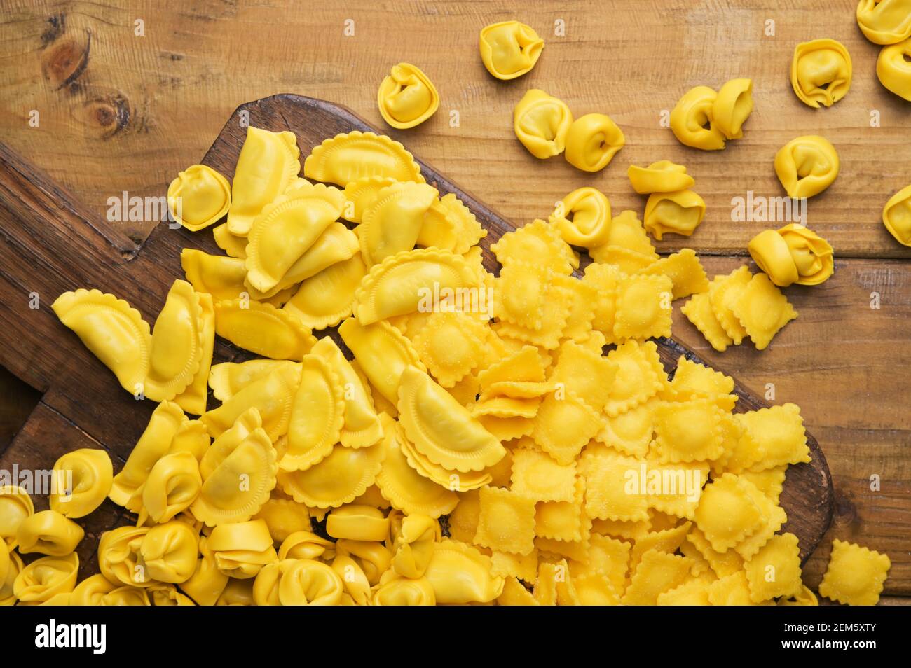Tartollini mit Käse oder Fleisch zum Kochen in Brühe, verschiedene Formen. Traditionelles Gericht für Feiern in italien, Emilia Romagna Region. Frische hausgemachte Pasta mit Füllung auf einem Holztisch. Oben Stockfoto