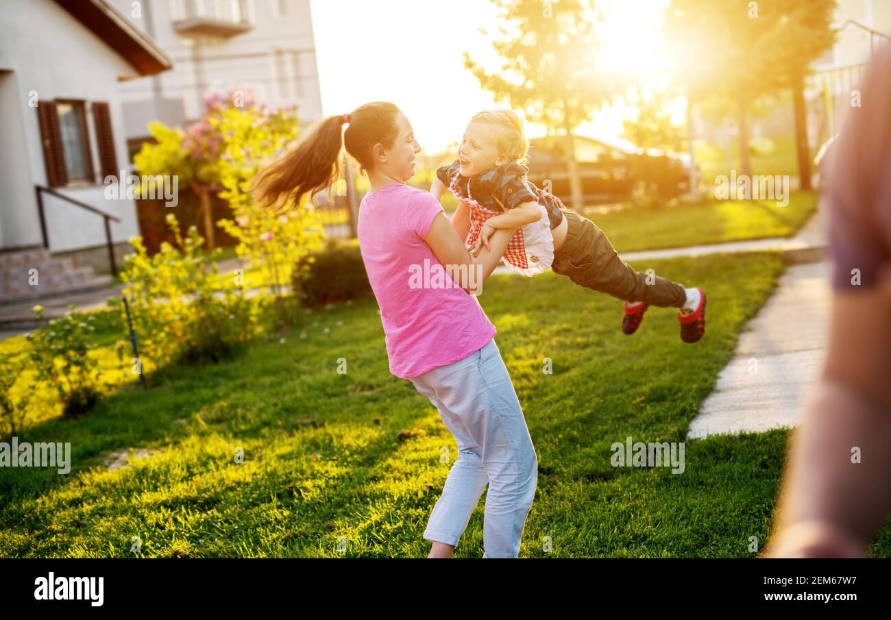 Junge fröhliche Mädchen hält ihre liebenswert Kleinkind Bruder und Spinnen ihn, während er kichert. Stockfoto