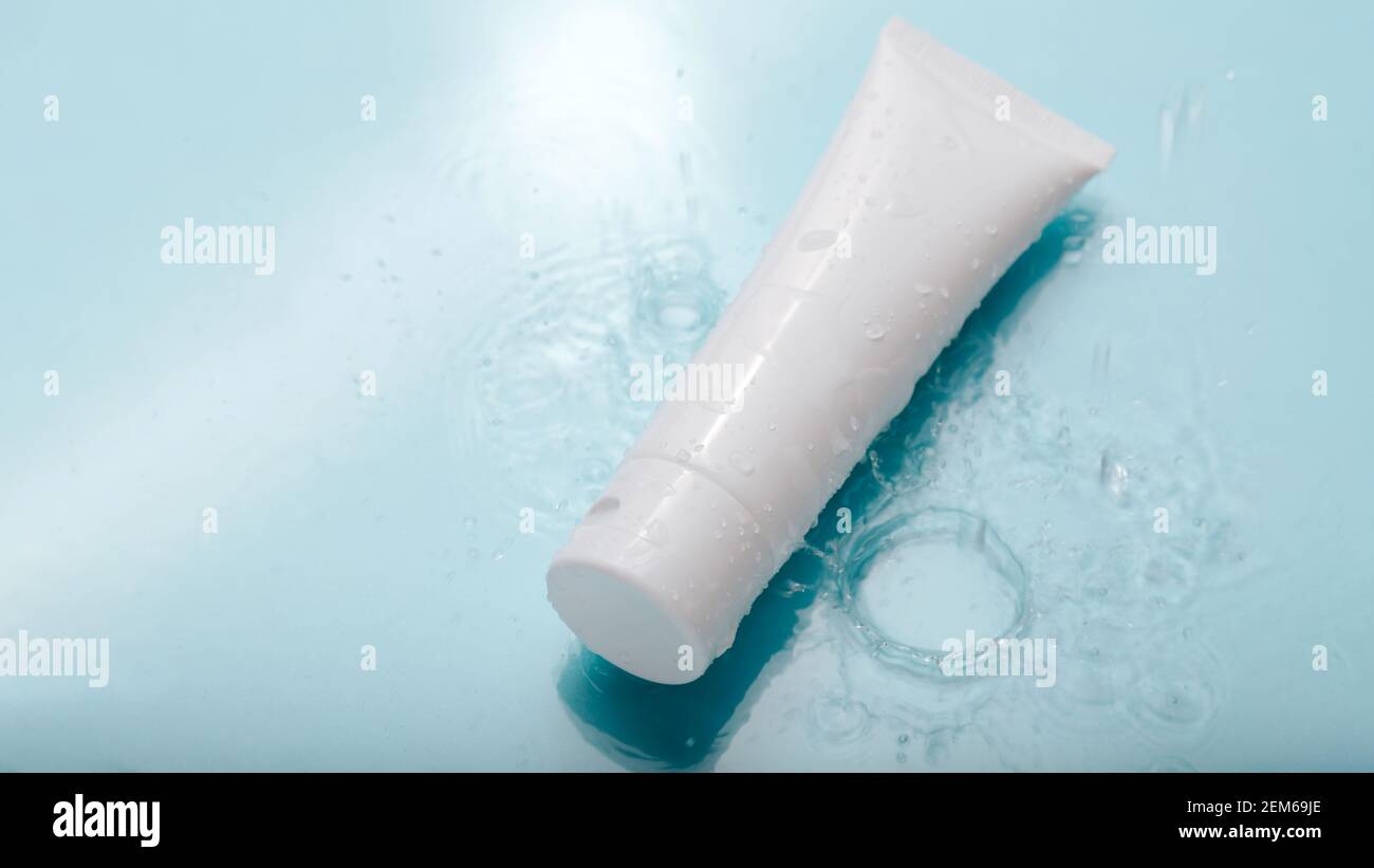 Weißes kosmetisches Produkt in Tube auf blauem Hintergrund mit Wassertropfen. Mock up Hautpflege Kosmetik-Paket auf Wasseroberfläche. Wasserhaushalt Kosmetik Stockfoto