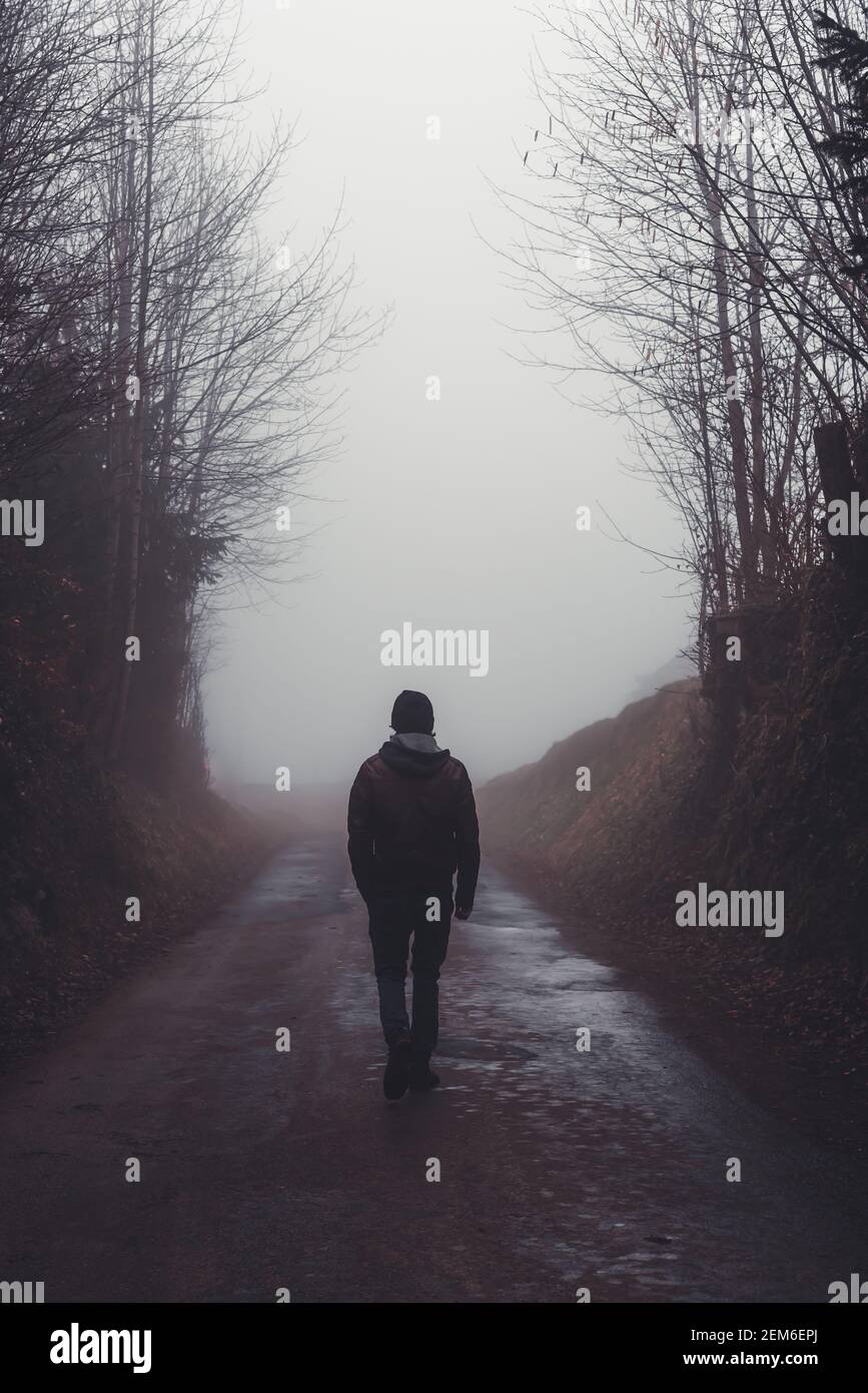 Mann, der alleine auf einer Straße durch einen dunklen Nebel geht Wald Stockfoto