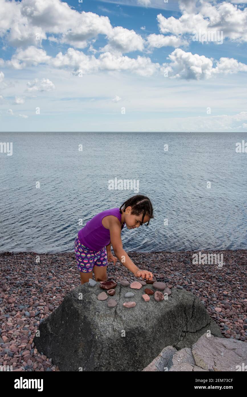 Duluth, Minnesota. 5-jährige bi-rassische Mädchen sammeln Felsen für ihre Sammlung, während im Urlaub am Lake Superior Nordufer. Stockfoto