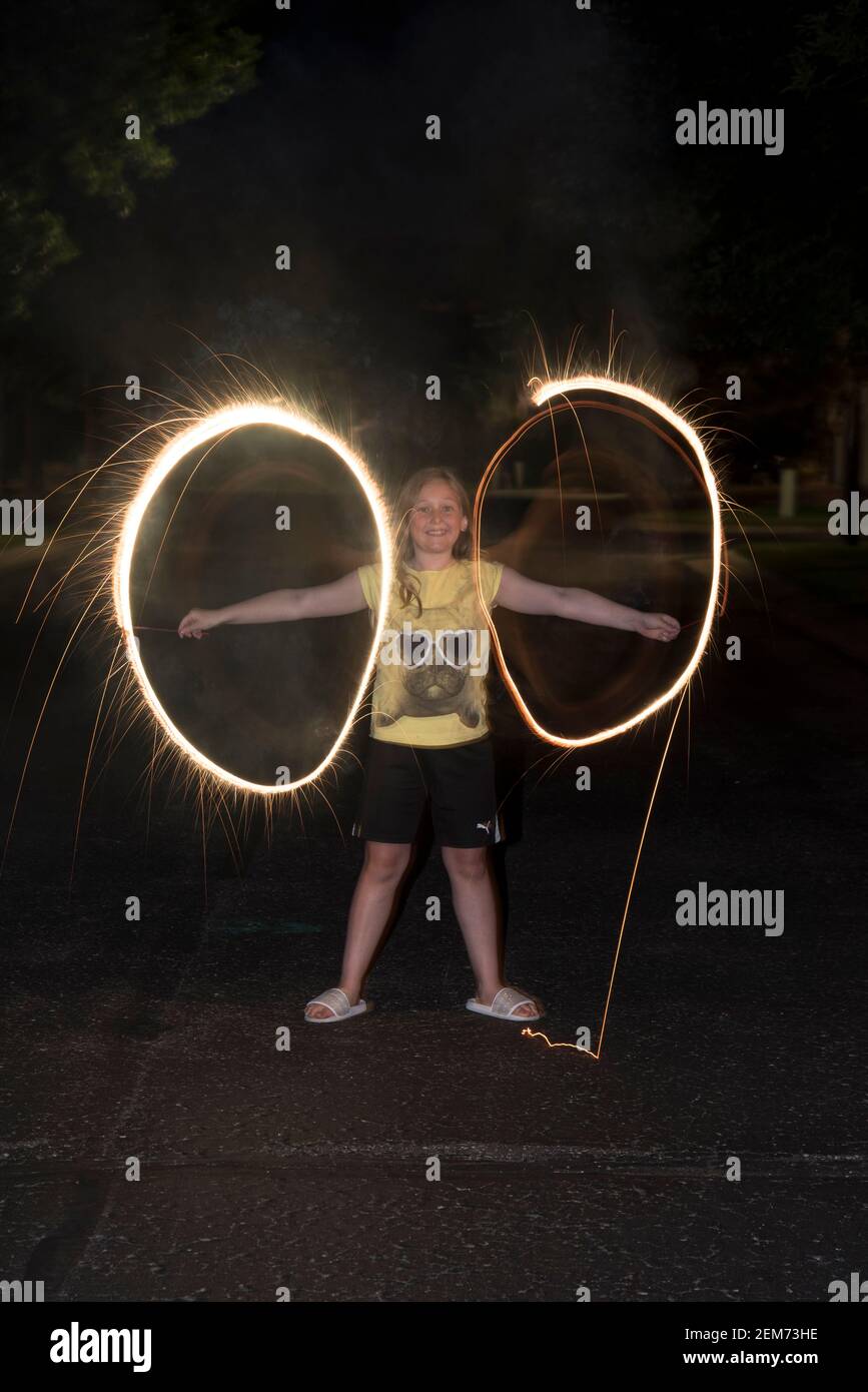 Vadnais Heights, Minnesota. 11-jähriges Mädchen spielt und wirbelt funkelndes Feuerwerk am Abend. Stockfoto