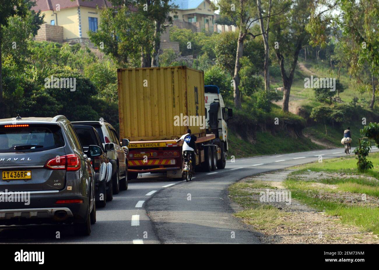 Ein Radfahrer in Ruanda hält sich an einen LKW und fängt eine Fahrt den Hügel hinunter. Stockfoto