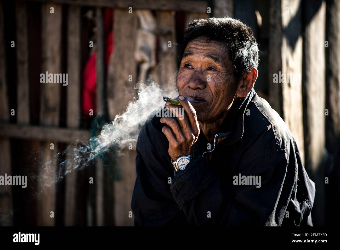 Chiang Mai / Thailand - Jan 16 2016 : der alte Asiate raucht und lächelt mit guter Laune, trägt alte Kleider, ein Bergstämmier in einem ländlichen Dorf in Nort Stockfoto