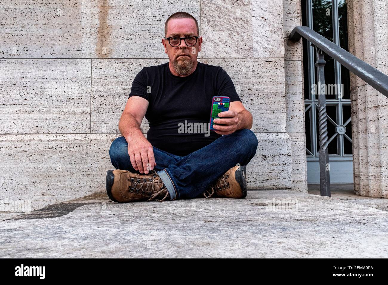 Porträt eines Reifen Erwachsenen, kaukasischen Mannes, der an einer grauen Wand sitzt. Berlin, Deutschland. Stockfoto