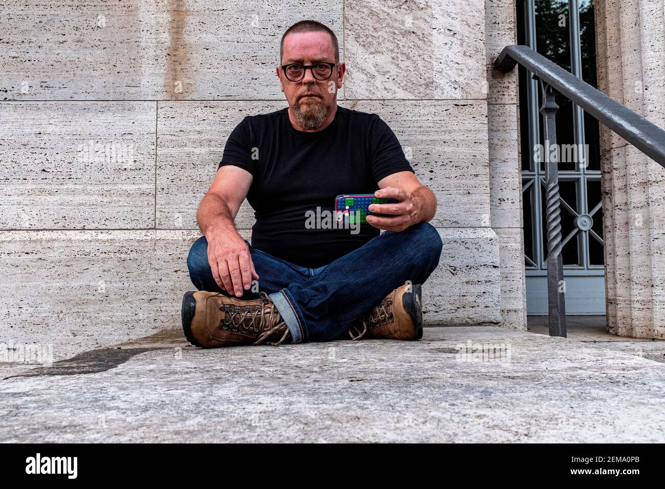 Berlin, Deutschland, Porträt eines erwachsenen, kaukasischen Mannes, der an einer grauen Wand sitzt. Stockfoto
