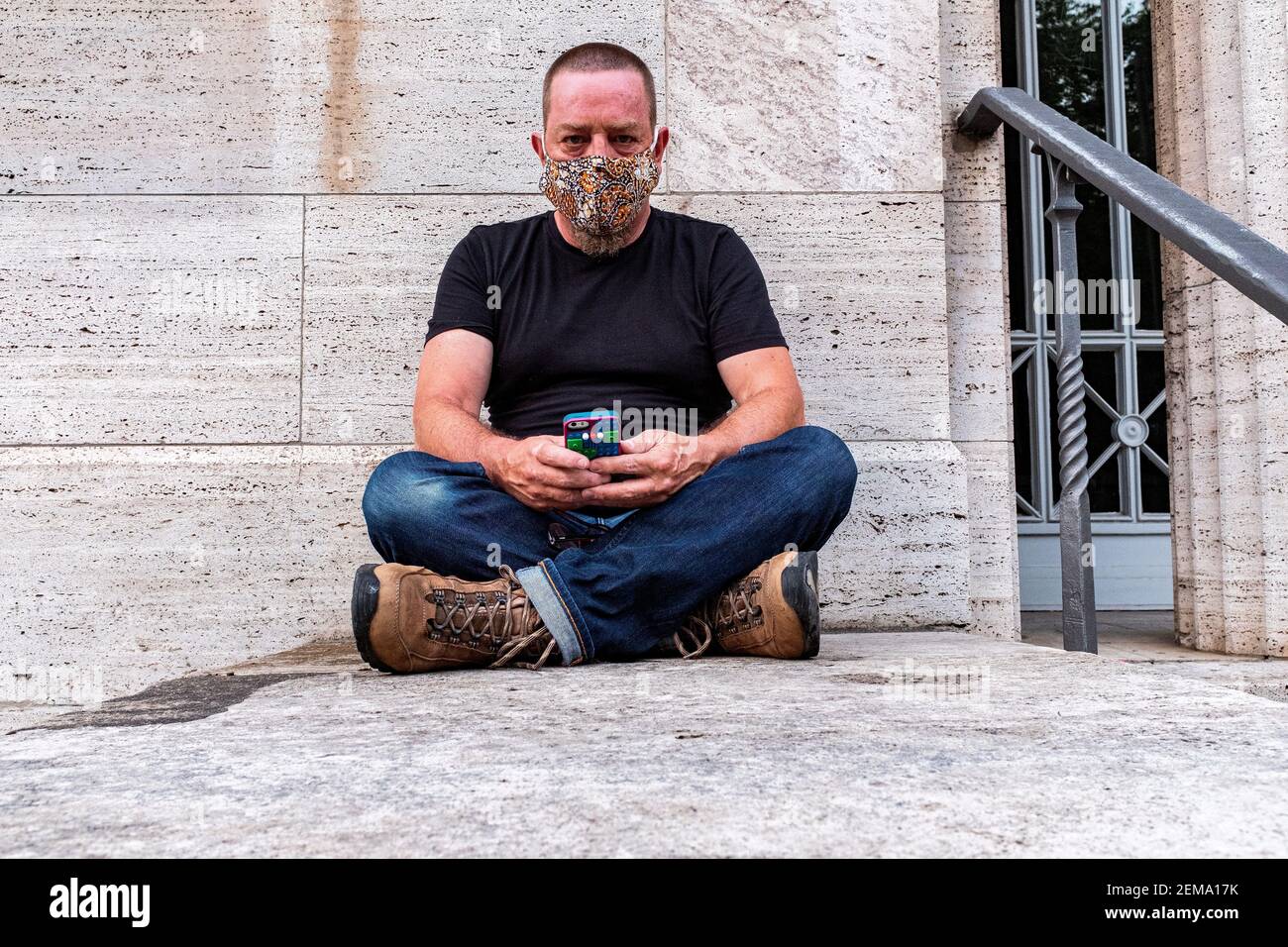 Berlin, Deutschland, Porträt eines erwachsenen, kaukasischen Mannes, der an einer grauen Wand sitzt. Stockfoto