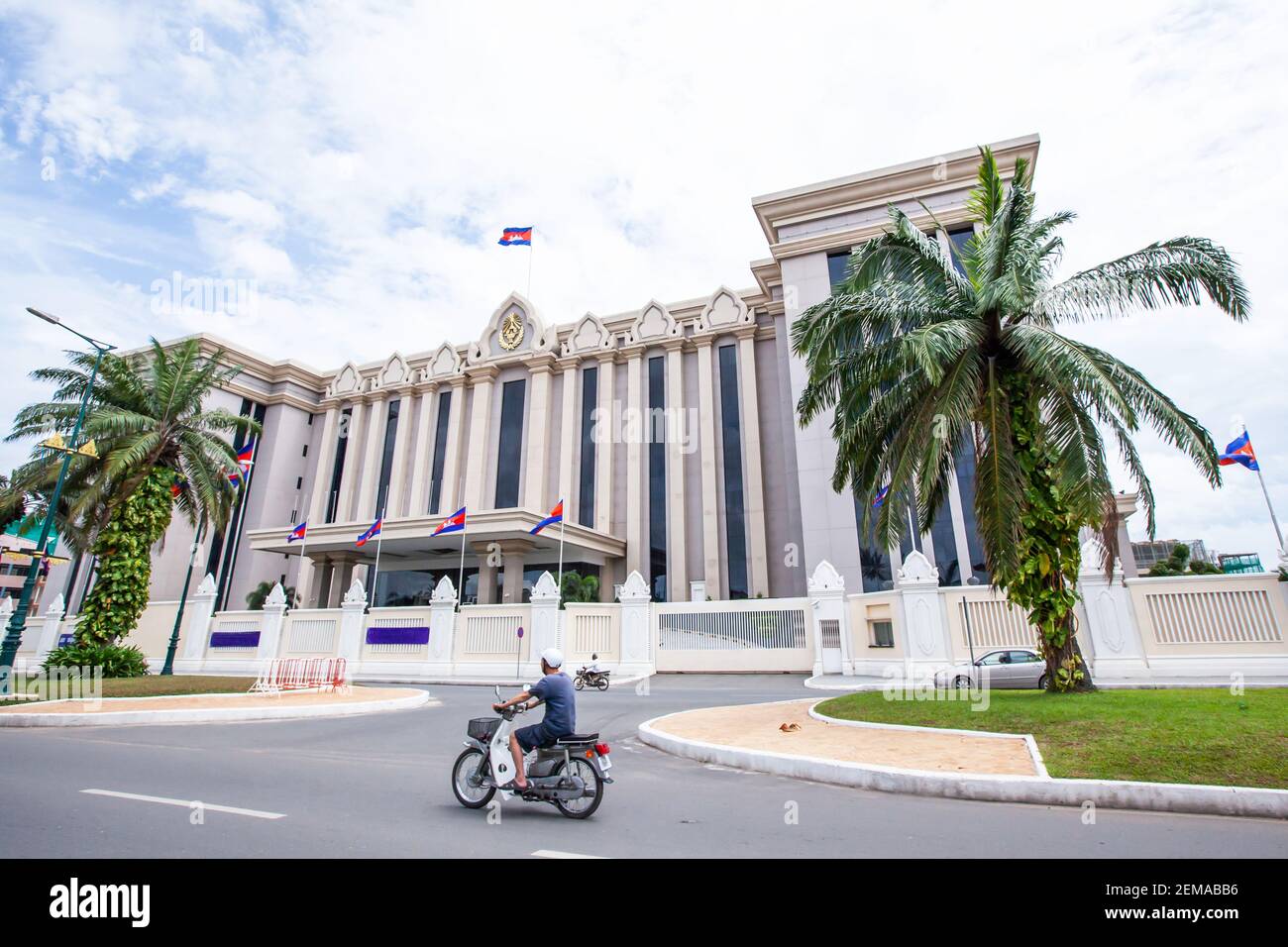 Khmer Leute fahren Motorrad passieren die Royal Government Hall von Kambodscha an sonnigen Tag. Es ist das erste moderne Regierungsgebäude nach dem Bürgerkrieg Stockfoto