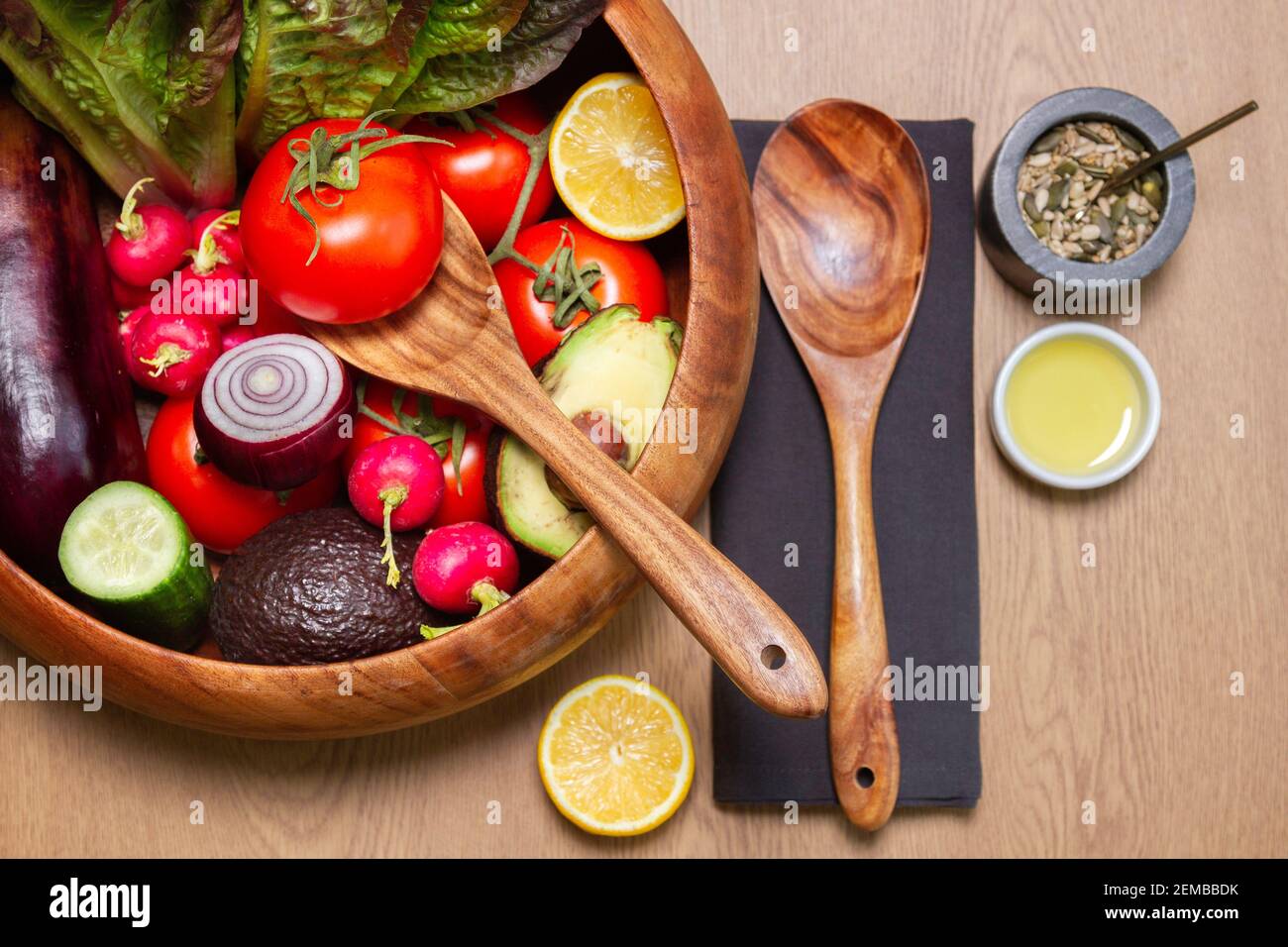 Holzsalatschüssel und Kellner mit allen Zutaten der Reihe Mit schwarzen Servietten und etwas Öl mit Samen gemischt Stockfoto