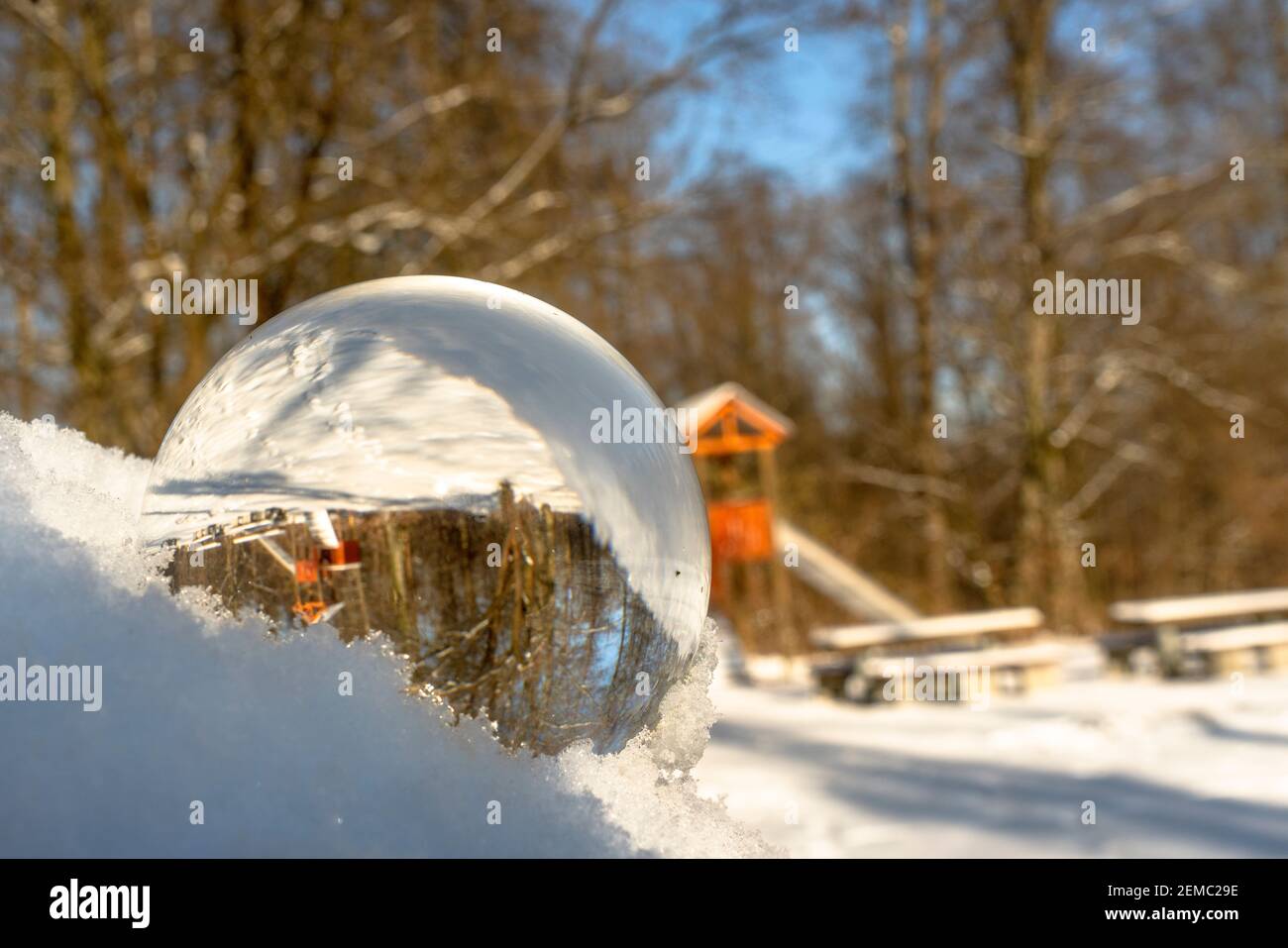 Glaskugel oder Linsenball im Schnee. Der Hintergrund mit Bäumen und anderen Objekten spiegelt sich in der Glaskugel Stockfoto