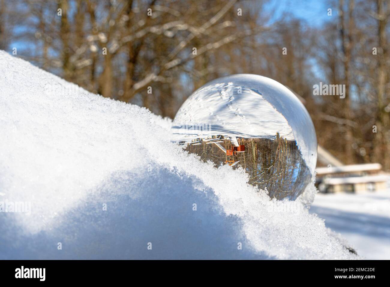 Glaskugel oder Linsenball im Schnee. Der Hintergrund mit Bäumen und anderen Objekten spiegelt sich in der Glaskugel Stockfoto