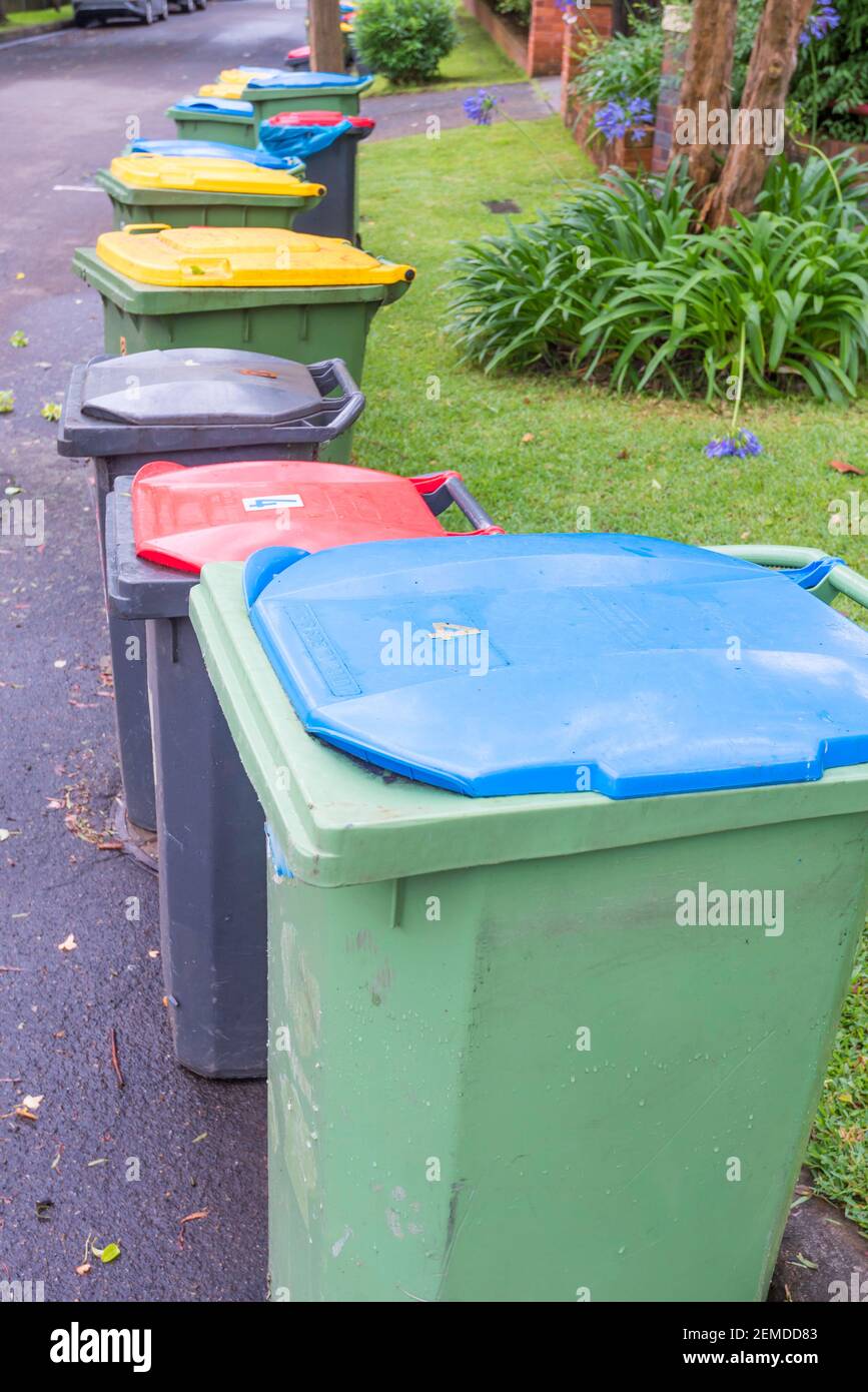 Rote (Deponie), blaue (Papier) und gelbe (comingled) lidded Abfall oder Müll oder Mülltonnen vor einem Haus in Sydney am Abholtag aufgereiht Stockfoto