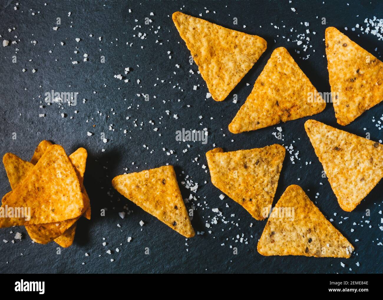 Hintergrund für das Essen. Gelbe dreieckige Tortilla Chips auf schwarz. Mexikanische salzige Snack Basis von Mais. Leckere Nachos als Vorspeise. Traditionelle knusprige Cor Stockfoto