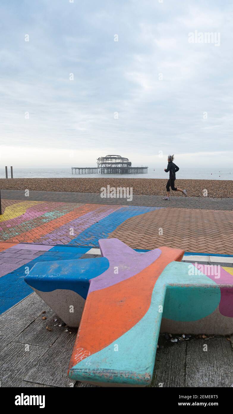 Brighton UK 25th February 2021 - EIN Läufer kommt an Brighton's West Pier an einem ruhigen trüben bewölkten Morgen entlang der Sussex Küste vorbei, aber sonniges Wetter wird für die nächsten Tage prognostiziert : Credit Simon Dack / Alamy Live News Stockfoto