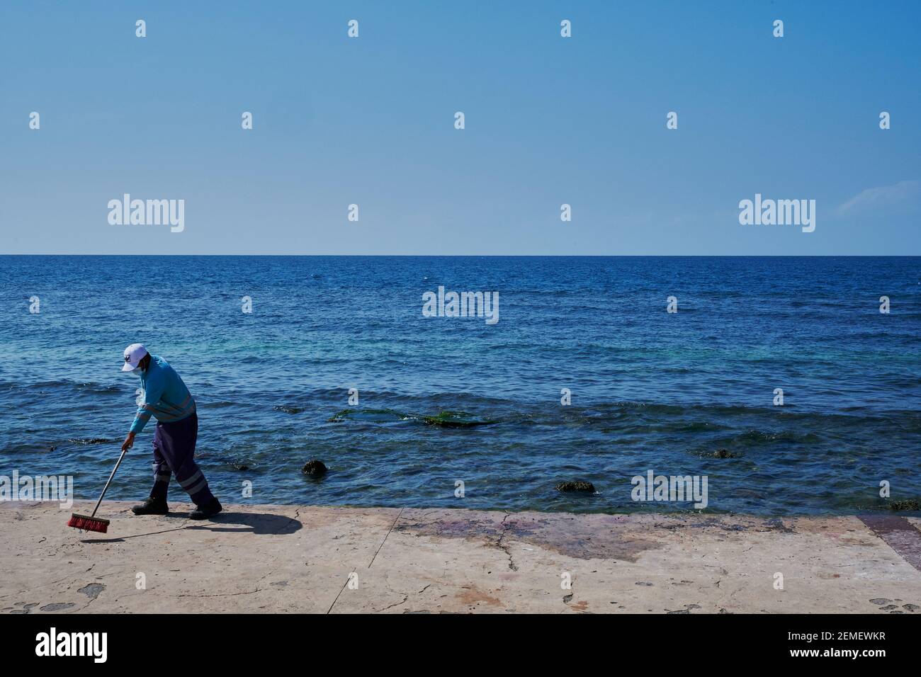 Ein Mann fegen die corniche mit dem Meer in der Hintergrund, als hätte er unendliche Arbeit Stockfoto