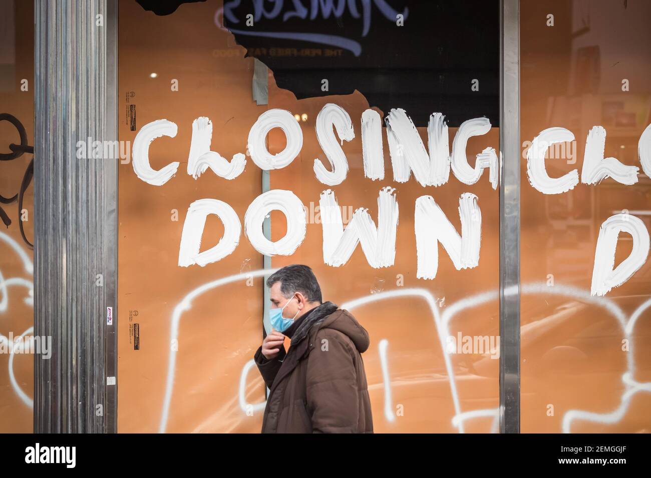 London, Großbritannien - 5. Februar 2021 - Schließen Sie ein Schild an einem Schaufenster, während ein Mann mit einer schützenden Gesichtsmaske auf der Wood Green High Street vorbei geht Stockfoto