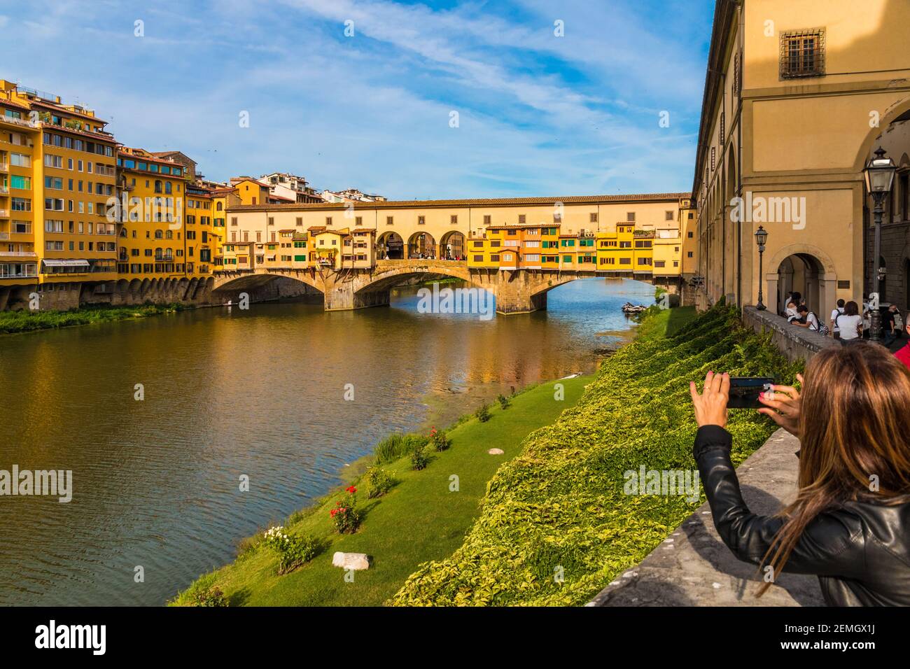 Eine Frau macht ein Foto mit ihrem Handy von der Brücke Ponte Vecchio, berühmt für die Geschäfte entlang der Brücke über den Arno im historischen Zentrum gebaut Stockfoto