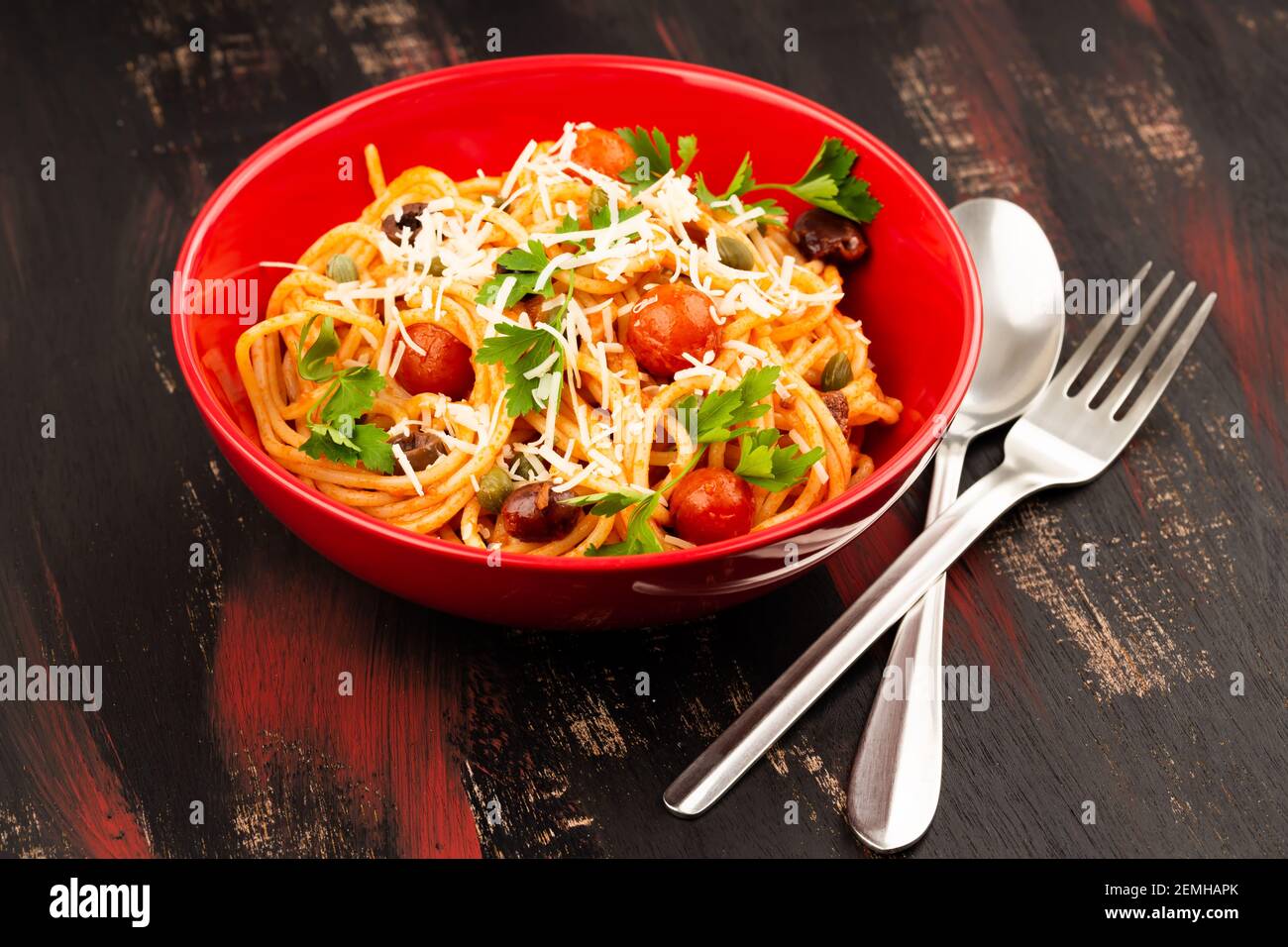 Pasta Spaghetti Puttanesca in roter Schale auf buntem Holzhintergrund. Italienische Küche. Stockfoto
