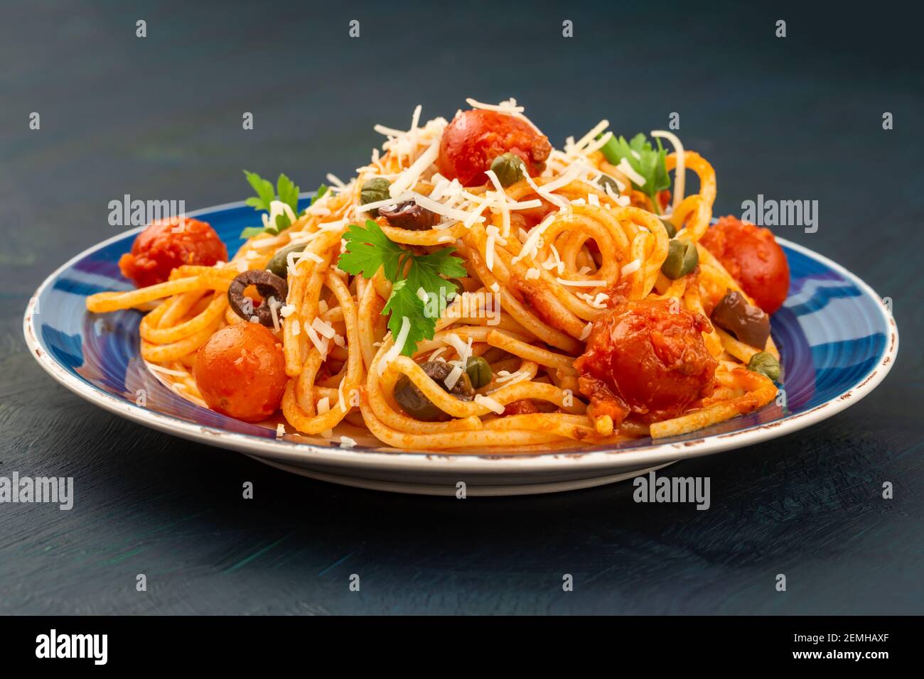 Pasta Spaghetti Puttanesca auf blauem Teller auf dunklem Holzhintergrund. Italienische Küche. Stockfoto