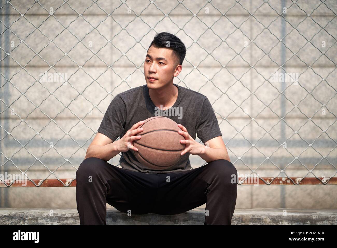 Junge asiatische Basketballspieler hält einen Ball sitzen bei ruhen courtside Stockfoto
