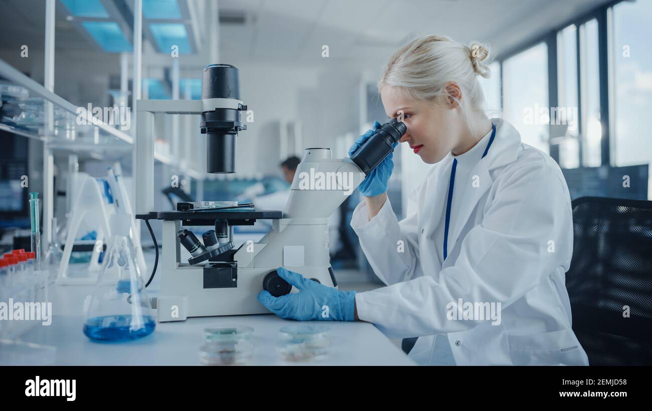 Modernes medizinisches Forschungslabor: Portrait einer Wissenschaftlerin, die unter dem Mikroskop schaut und Biochemikalien analysiert. Advanced Scientific Lab für Stockfoto