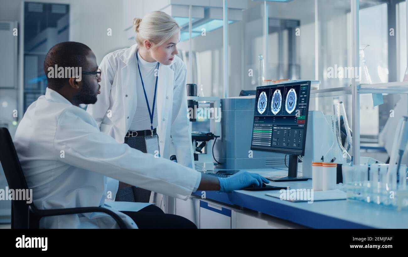Modernes medizinisches Forschungslabor: Zwei Wissenschaftler nutzen Computer mit Bildschirm MRT-Untersuchungen im Gehirn, Spezialisten diskutieren innovative Technologie Stockfoto