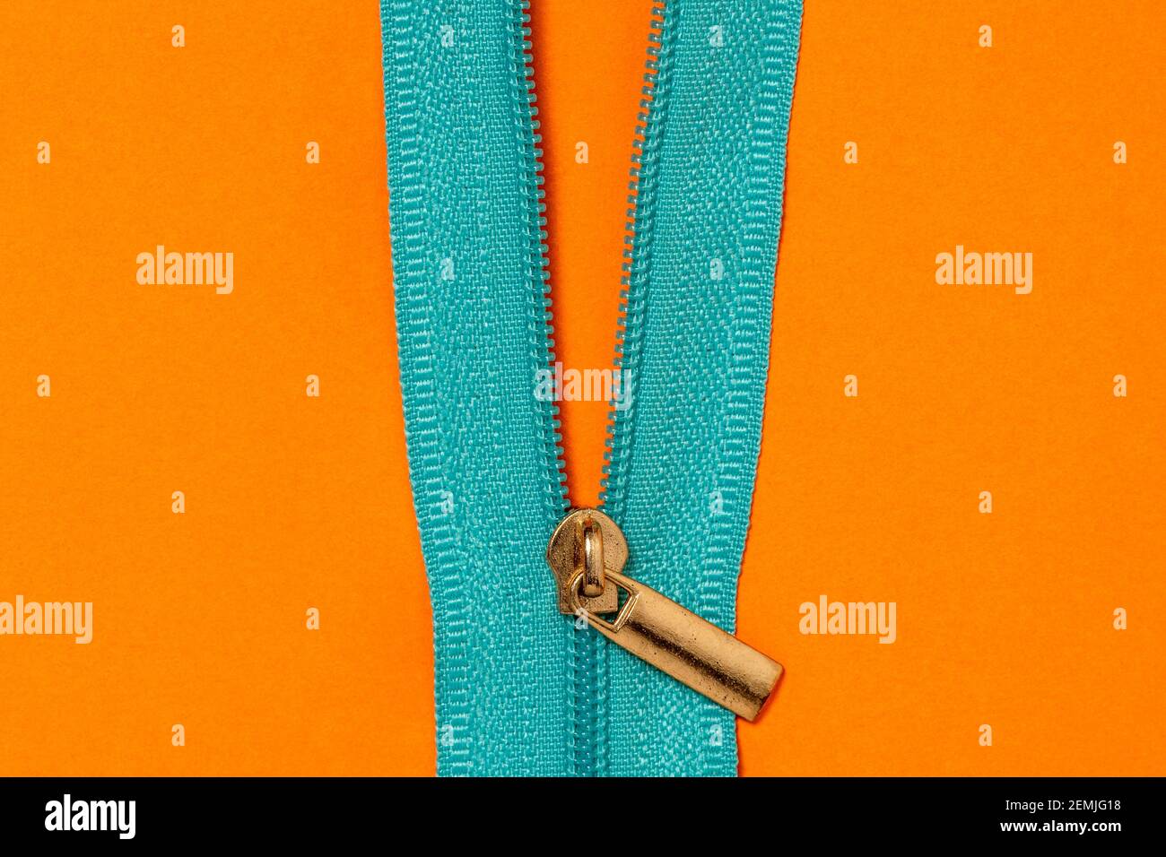 Nahaufnahme von entzipptem blauen Reißverschluss auf orangefarbenem Hintergrund Stockfoto