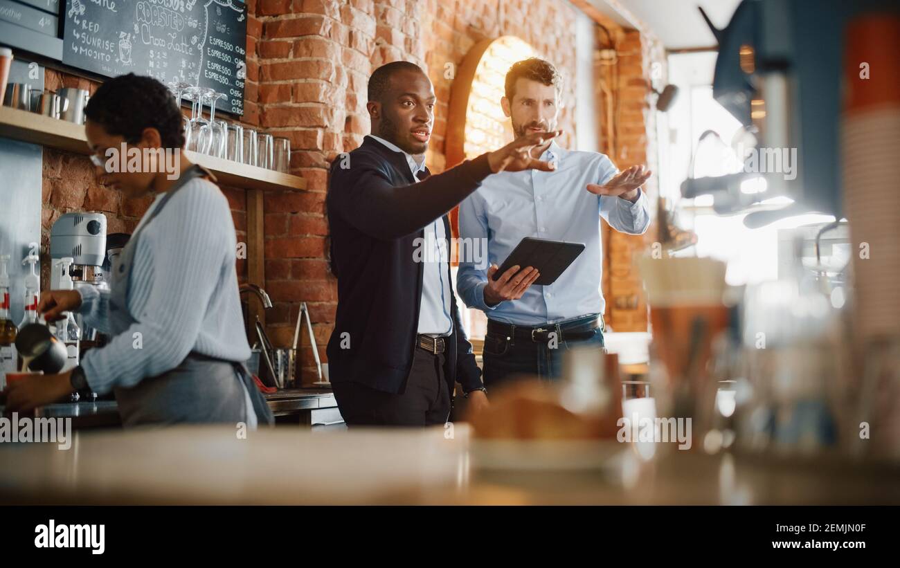 Multikulturelle Coffee Shop Besitzer Treffen hinter dem Counter und arbeiten Auf Tablet-Computer und Inventarkontrolle im gemütlichen Loft-Style Café Stockfoto