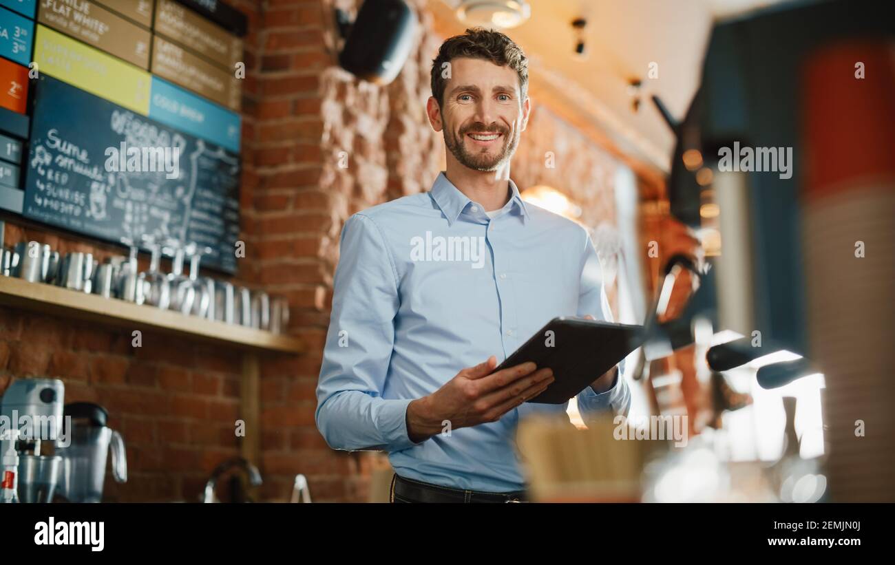 Handsome Caucasian Coffee Shop Besitzer arbeitet an Tablet-Computer und Überprüfung Inventar in einem gemütlichen Loft-Stil Cafe. Erfolgreicher Restaurantmanager Stockfoto