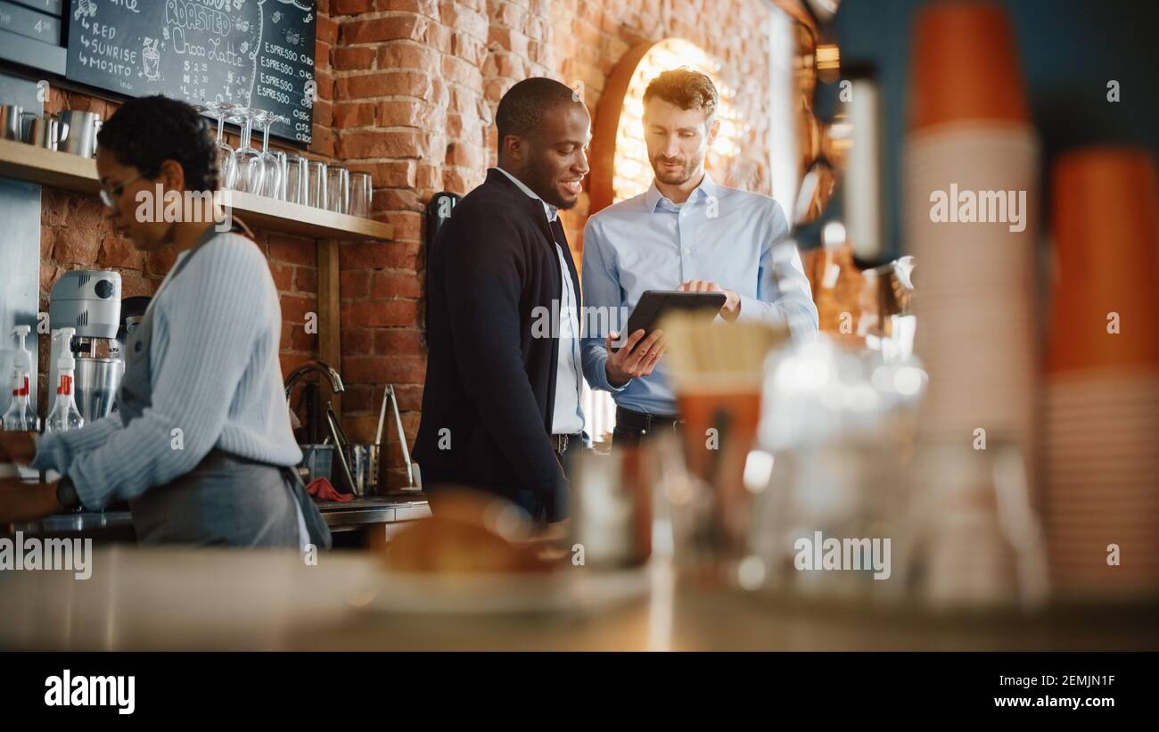 Multikulturelle Coffee Shop Besitzer Treffen hinter dem Counter und arbeiten Auf Tablet-Computer und Inventarkontrolle im gemütlichen Loft-Style Café Stockfoto