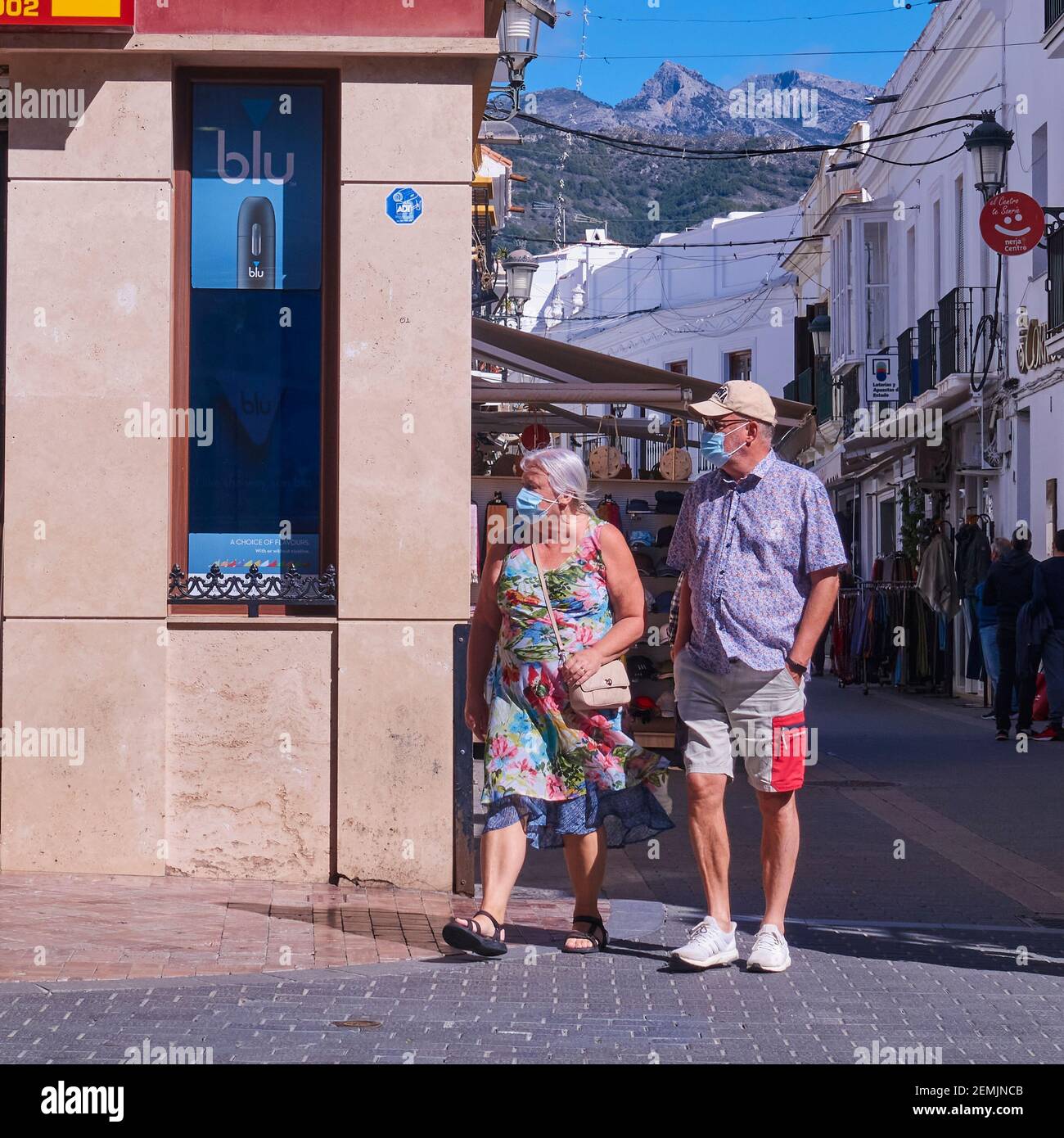 Vorderansicht eines Touristen-Paares, das Covid-Masken trägt, während sie durch die Costa del Sol-Resortstadt Nerja, Malaga, Spanien, laufen Stockfoto