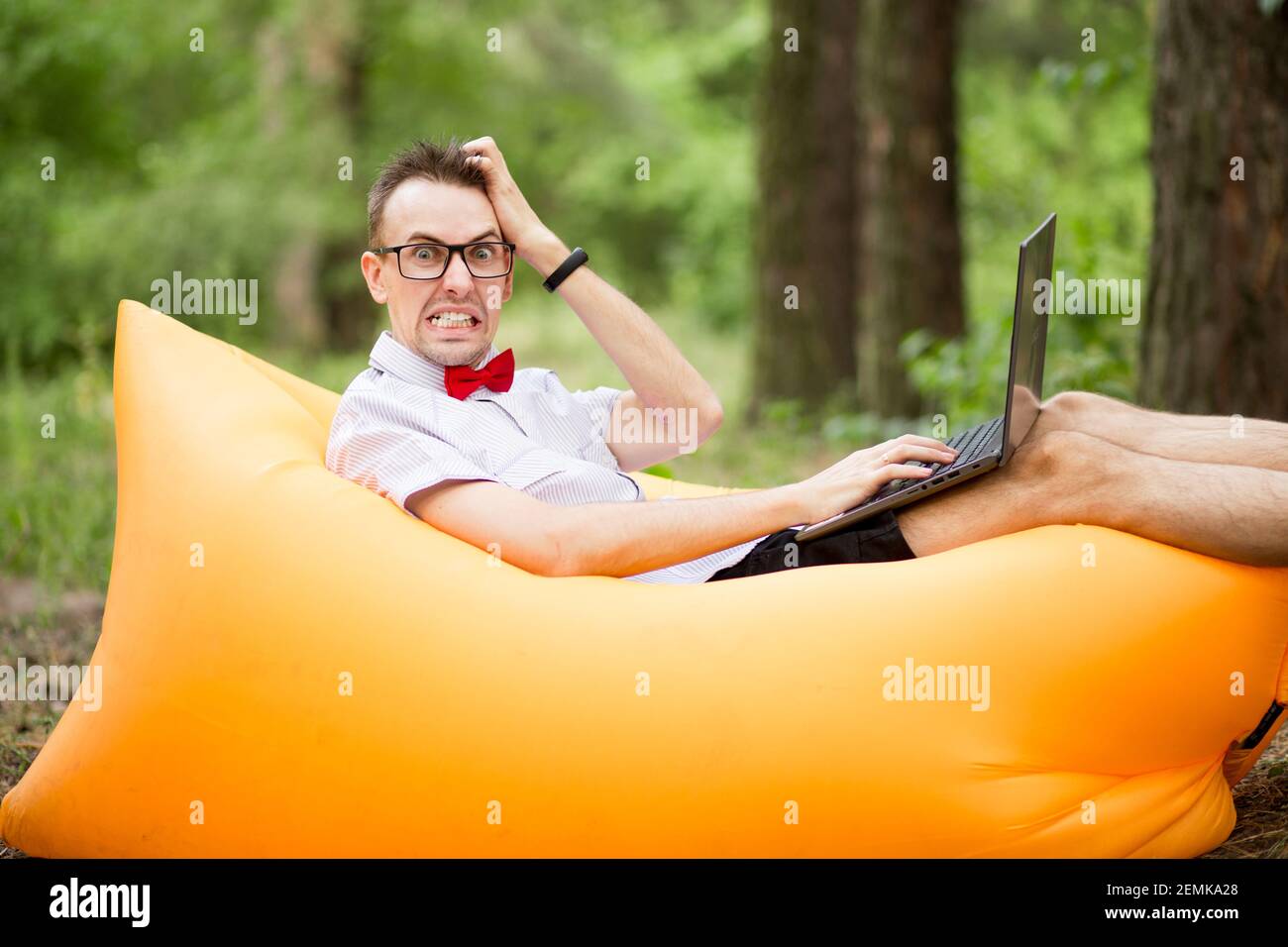 Erschrocken Student in Brille mit Laptop-Computer liegt auf aufblasbare Matratze im Sommer Park. Bildung, Geschäft, Ausfall und Technologiekonzept Stockfoto