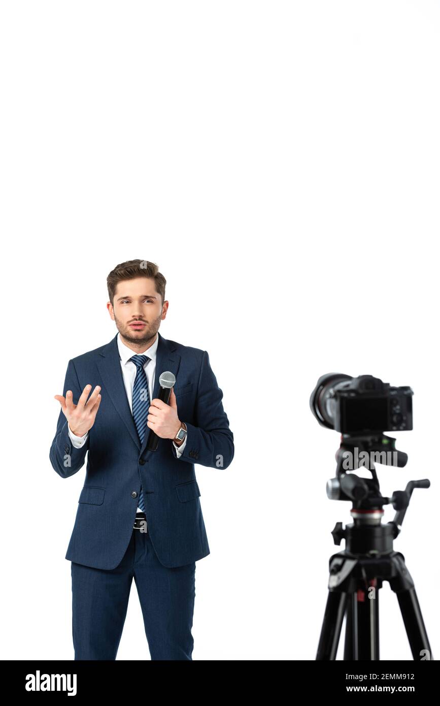 nachrichtenkommentator mit Mikrofon gestikulierende beim Sprechen in der Nähe von Digitalkamera Auf verschwommenem Vordergrund isoliert auf Weiß Stockfoto