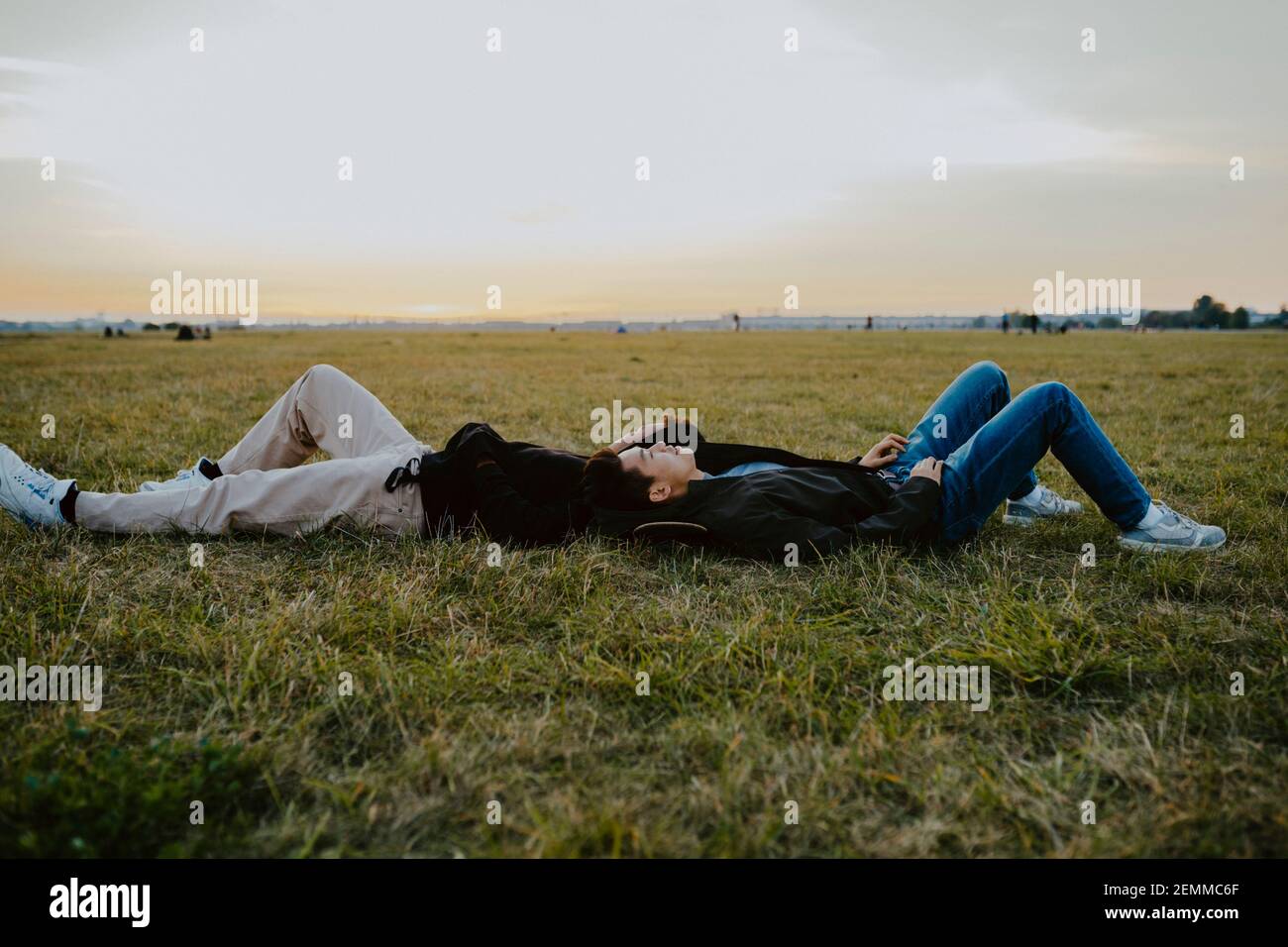 Männliche Freunde liegen auf Gras im Park während des Sonnenuntergangs Stockfoto