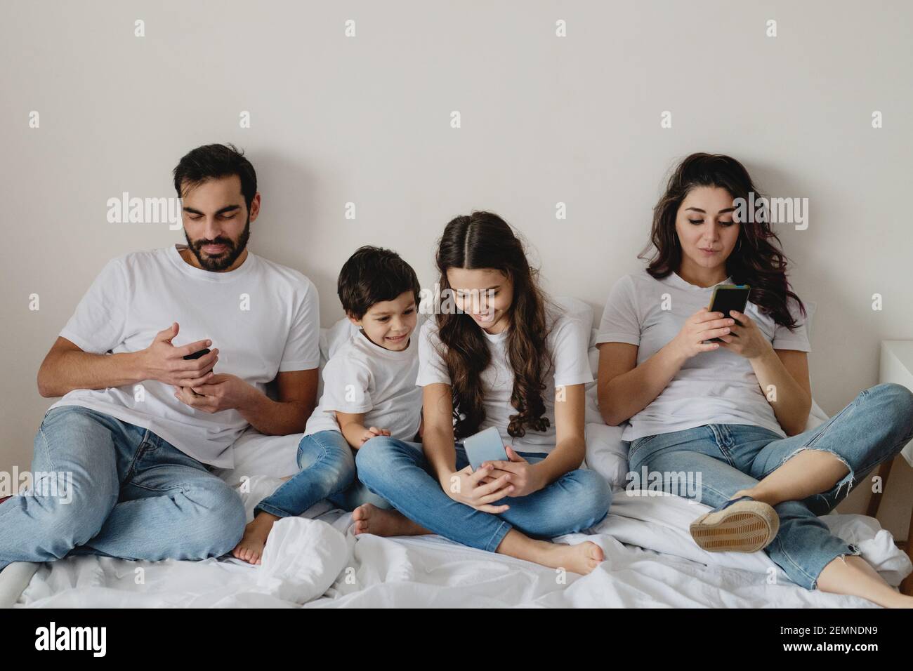 Familie im Bett mit Smartphones. Digitales technologieabhängiges Konzept. Stockfoto