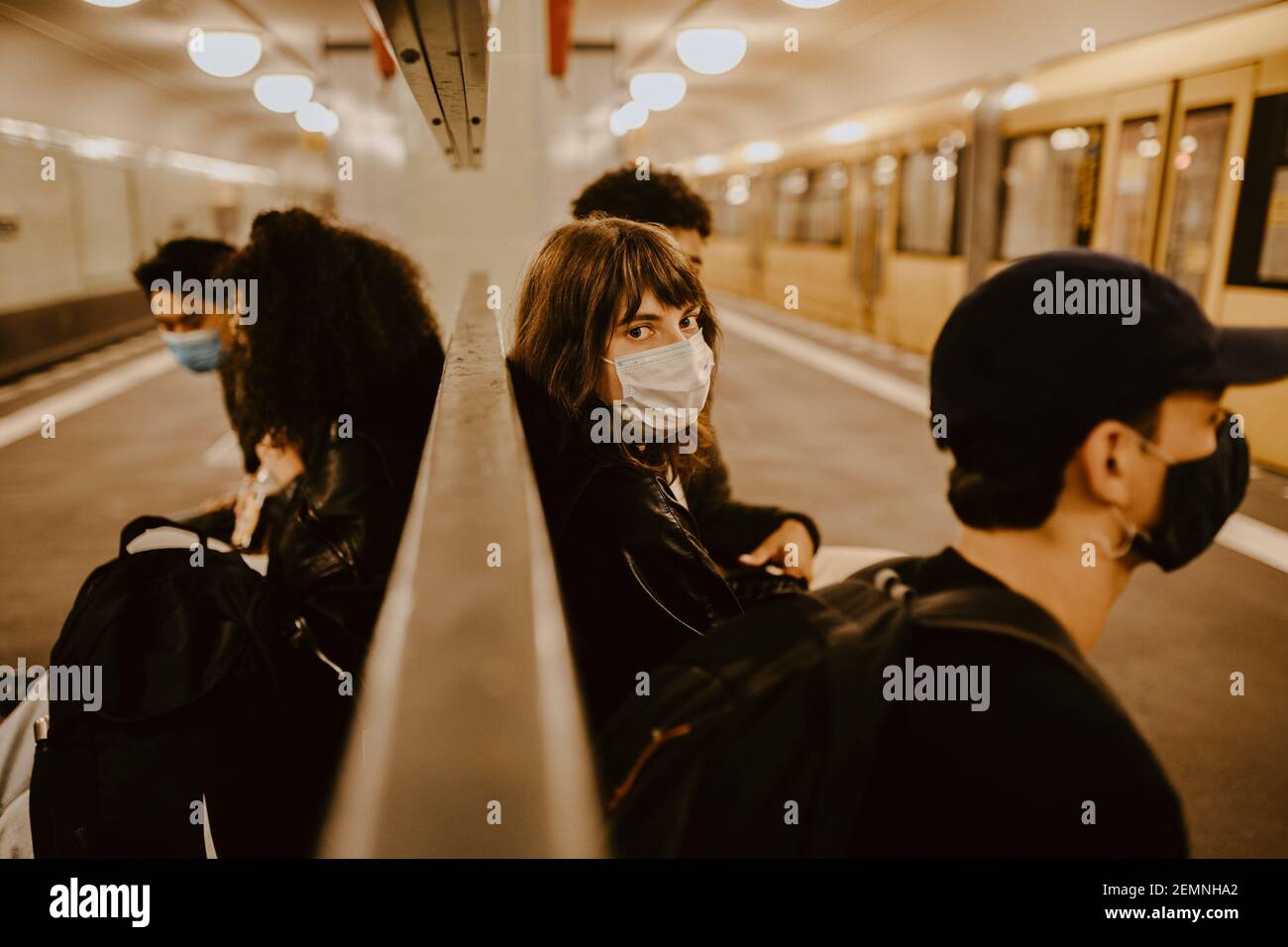 Junge Frau mit Freunden sitzen an U-Bahn-Station während Pandemie Stockfoto