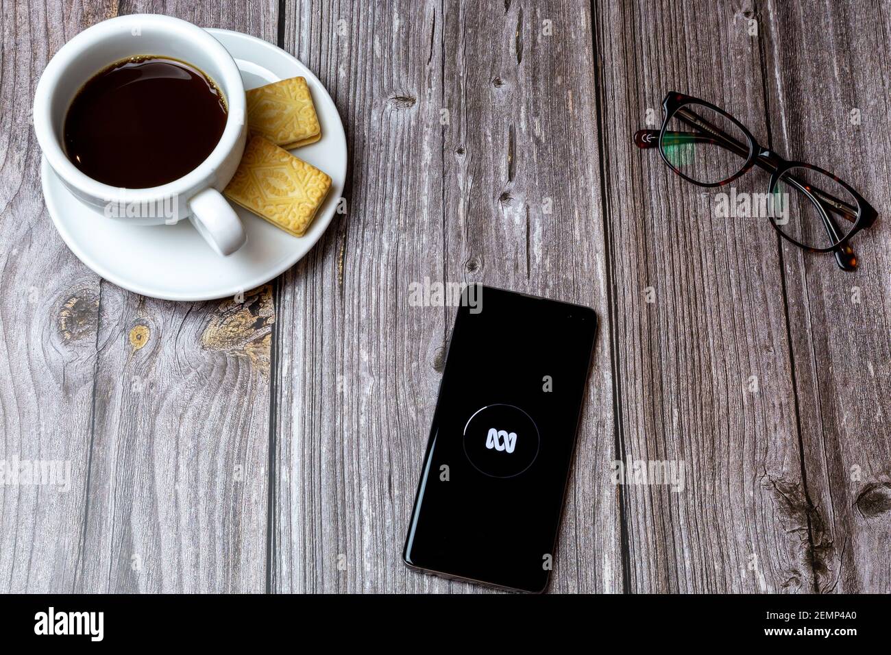 Ein Handy oder Handy auf einem Holztisch Mit der ABC News App neben einem Kaffee öffnen Und Brille Stockfoto