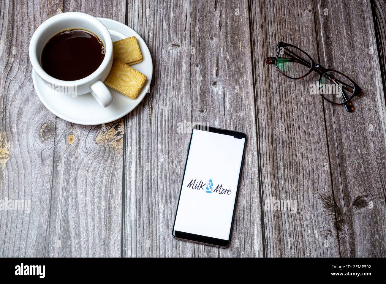 Ein Handy oder Handy auf einem Holztisch Mit der Milch und Mehr App geöffnet neben einem Kaffee und Gläser Stockfoto