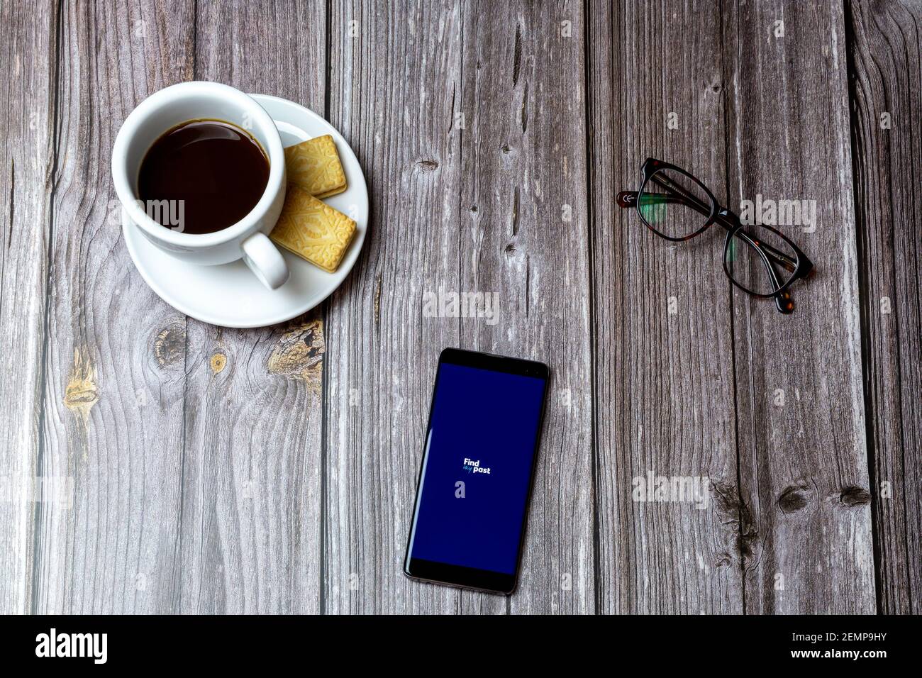 Ein Handy oder Handy auf einem Holztisch Mit der Find my past App geöffnet neben einem Kaffee und Gläser Stockfoto