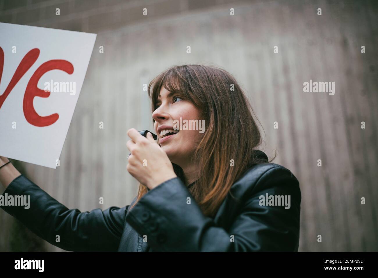Lächelnde Aktivistin mit Pfeife, die Plakat gegen die Wand hält Stockfoto