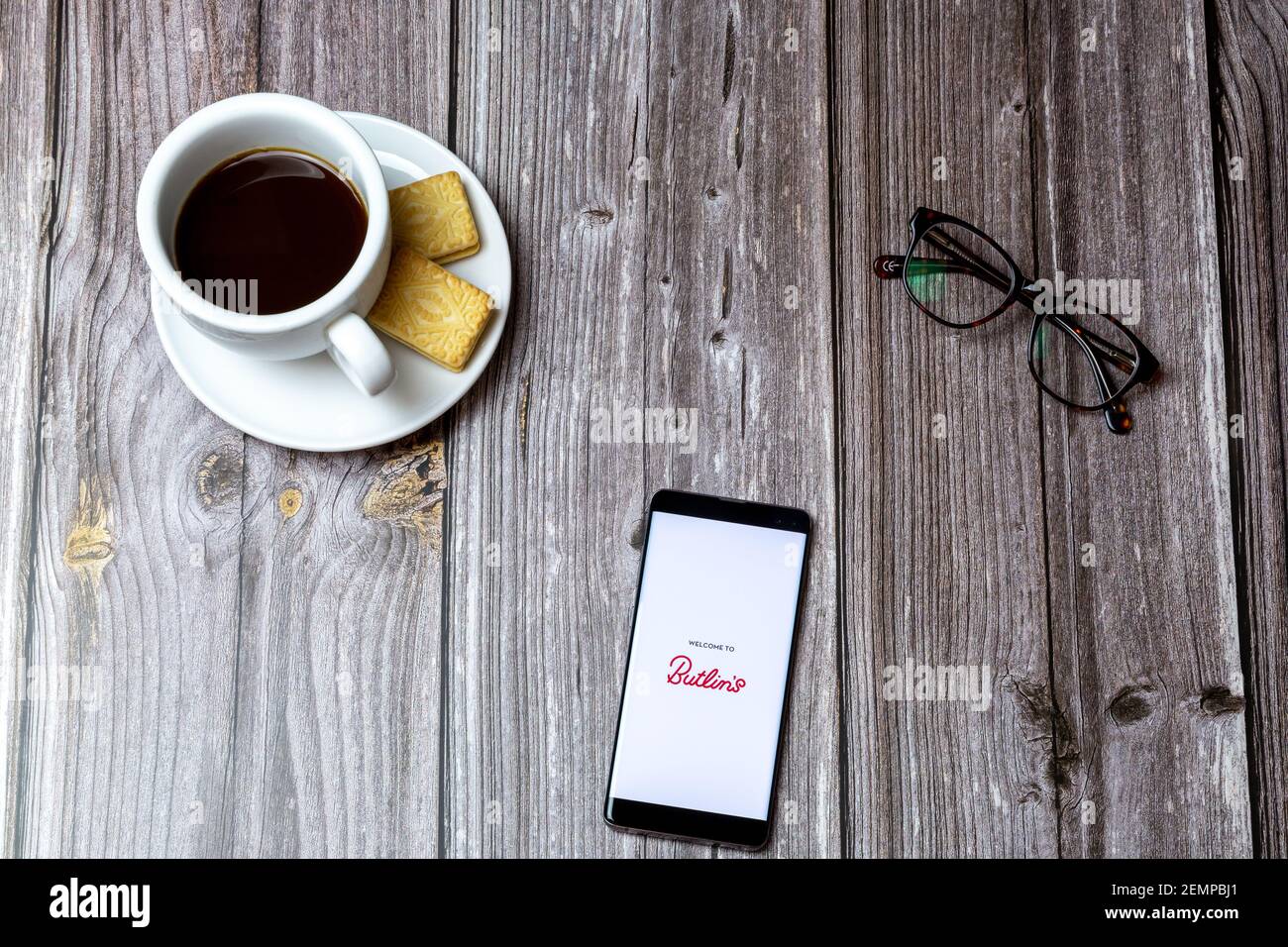 Ein Handy oder Handy auf einem Holztisch Mit der Butlins Holidays App neben einem Kaffee öffnen Und Brille Stockfoto