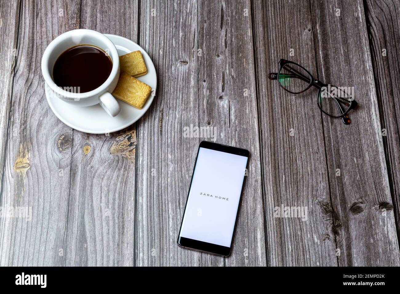 Ein Handy oder Handy auf einem Holztisch Mit der ZARA Home App neben einem Kaffee öffnen Und Brille Stockfoto