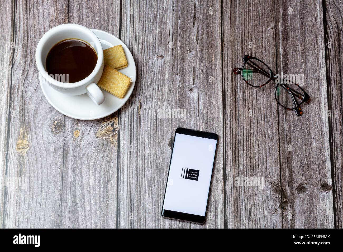 Ein Handy oder Handy auf einem Holztisch Mit der John Lewis and Partners App geöffnet neben Ein Kaffee Stockfoto
