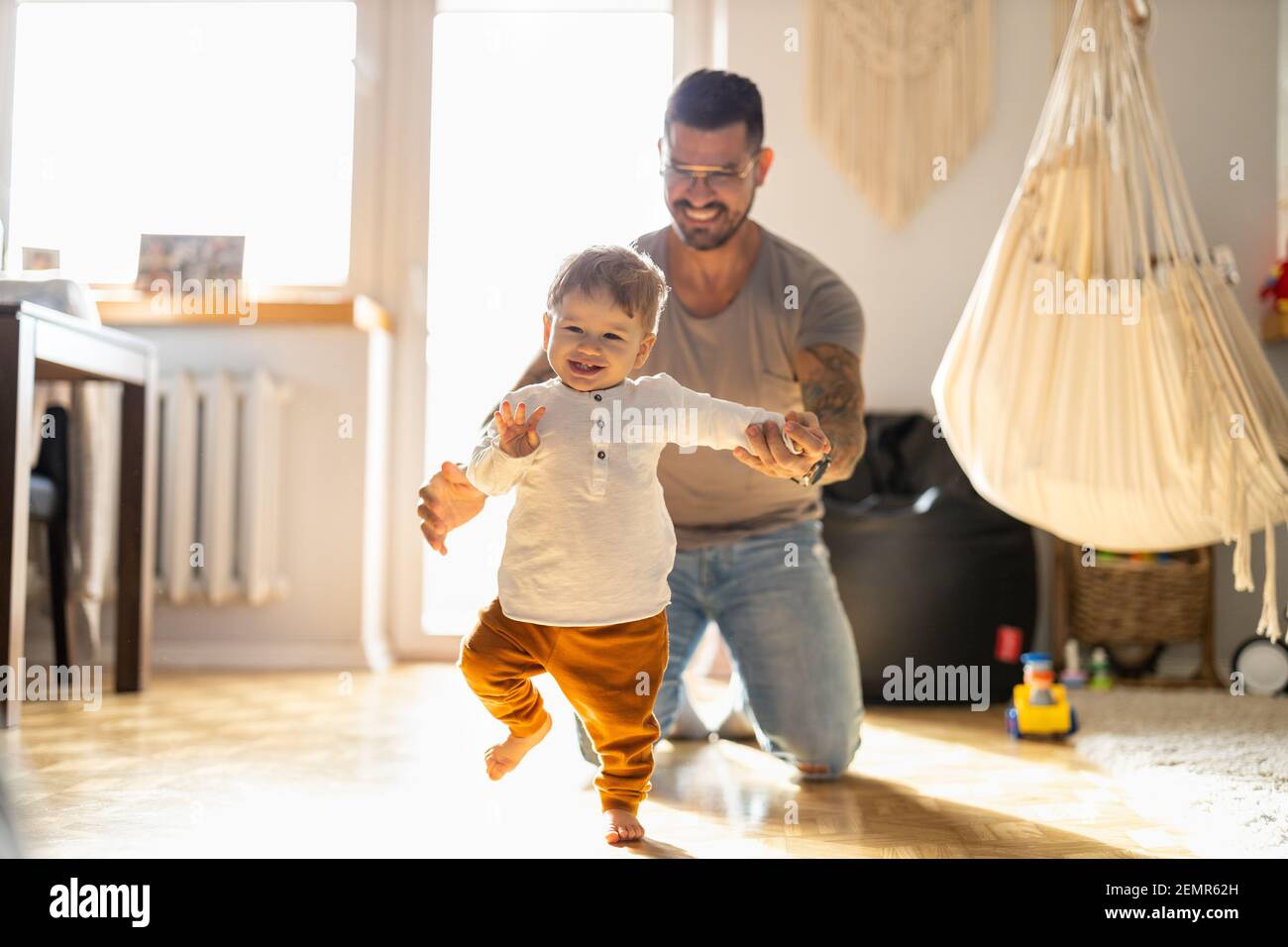 Glücklicher Vater hilft kleinen Sohn zu Fuß im Wohnzimmer Stockfoto