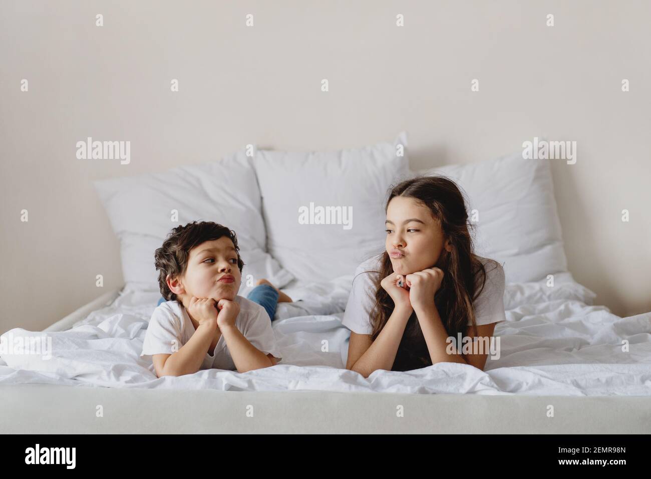 Netter kleiner Junge und seine Schwester schauen sich an, während sie auf einem Bett liegen. Stockfoto